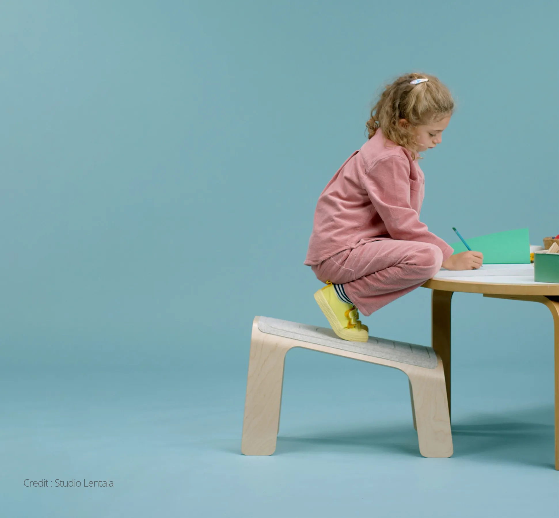 Young girl drawing at a table crouched on a wooden stool