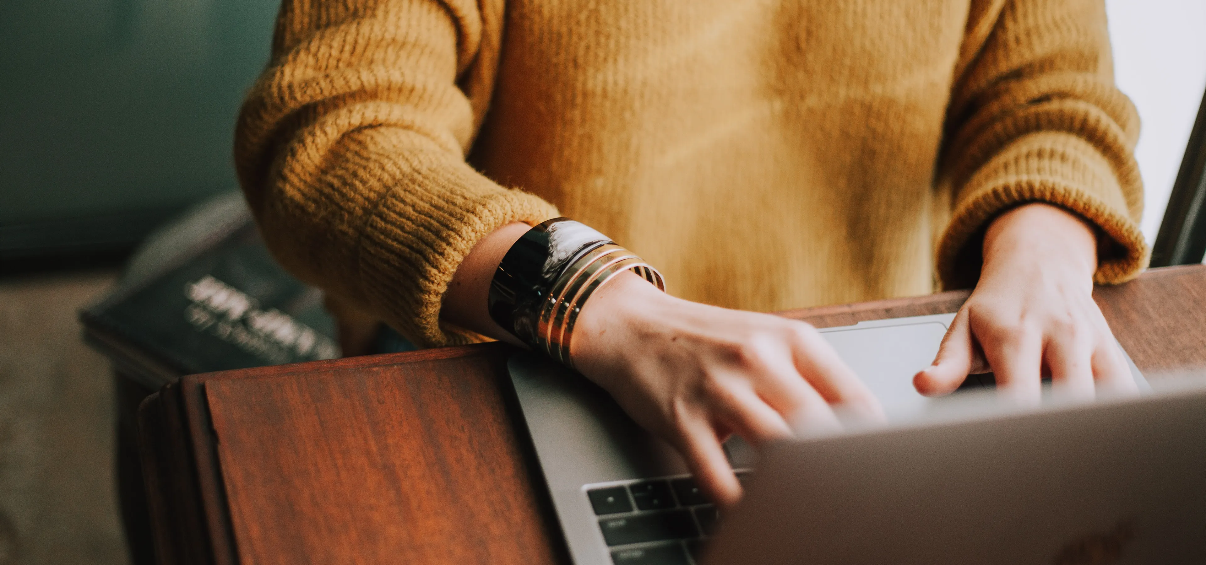 woman in yellow jumper typing at a laptop