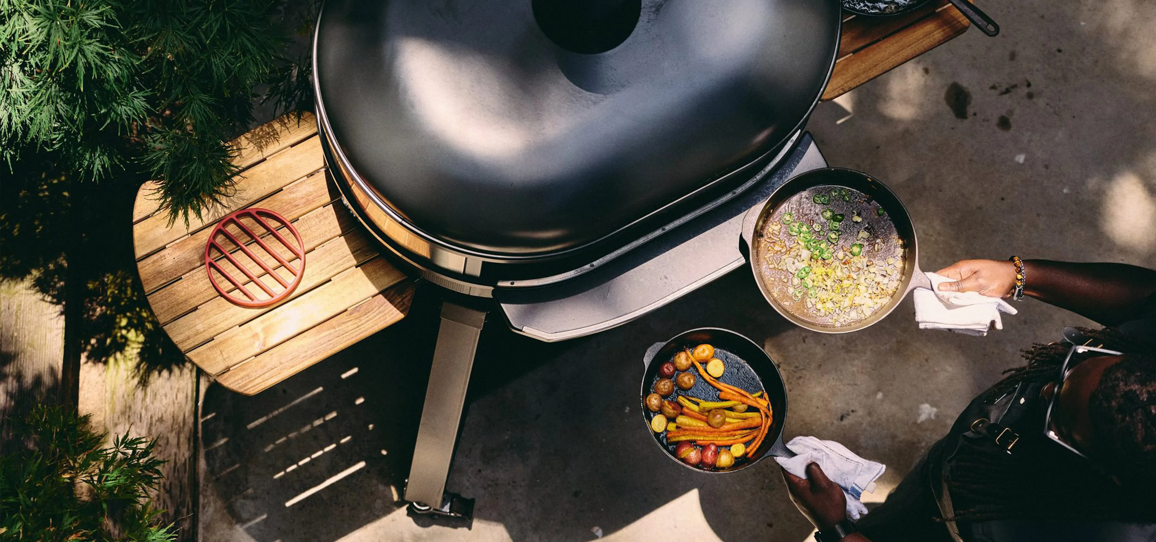 A person holding pans in front of an outdoor wood-fired cooker